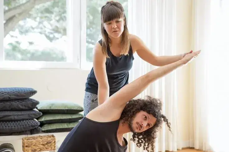Assisted yoga Instructor helping man to do side bend at yoga class